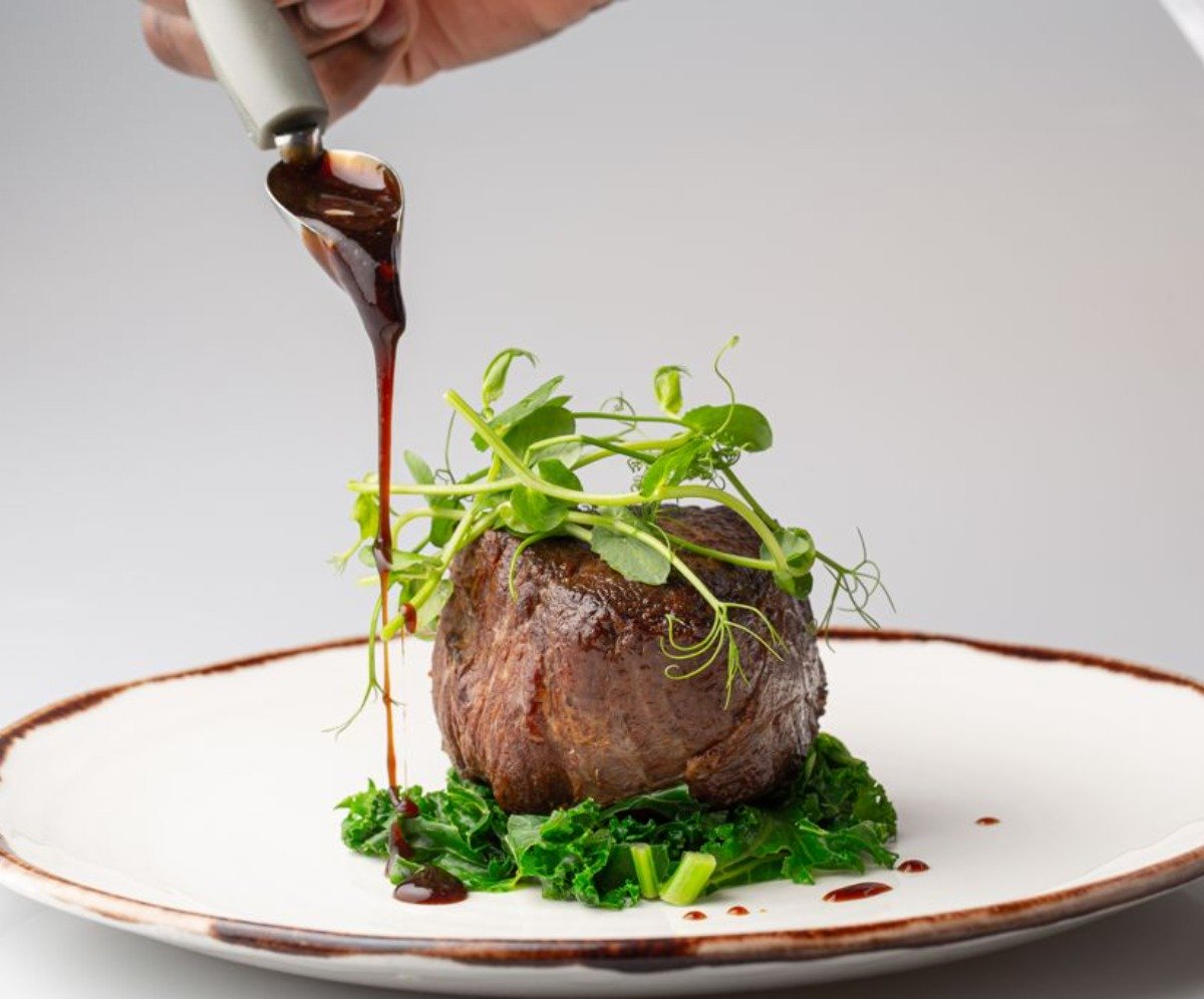 Private Jet Catering, with 3 Flavours Fillet steak on a white plate sat on kale and garnished with pea shoots, drizzled with a sauce